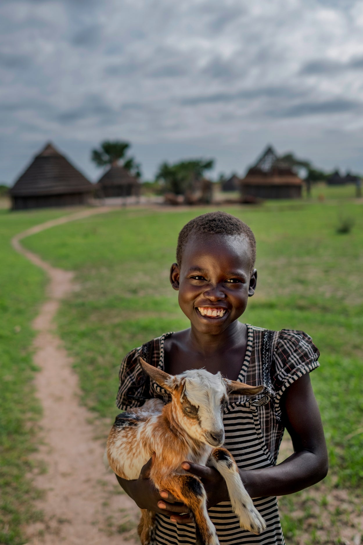 Girl holding a goat in front of a village road
