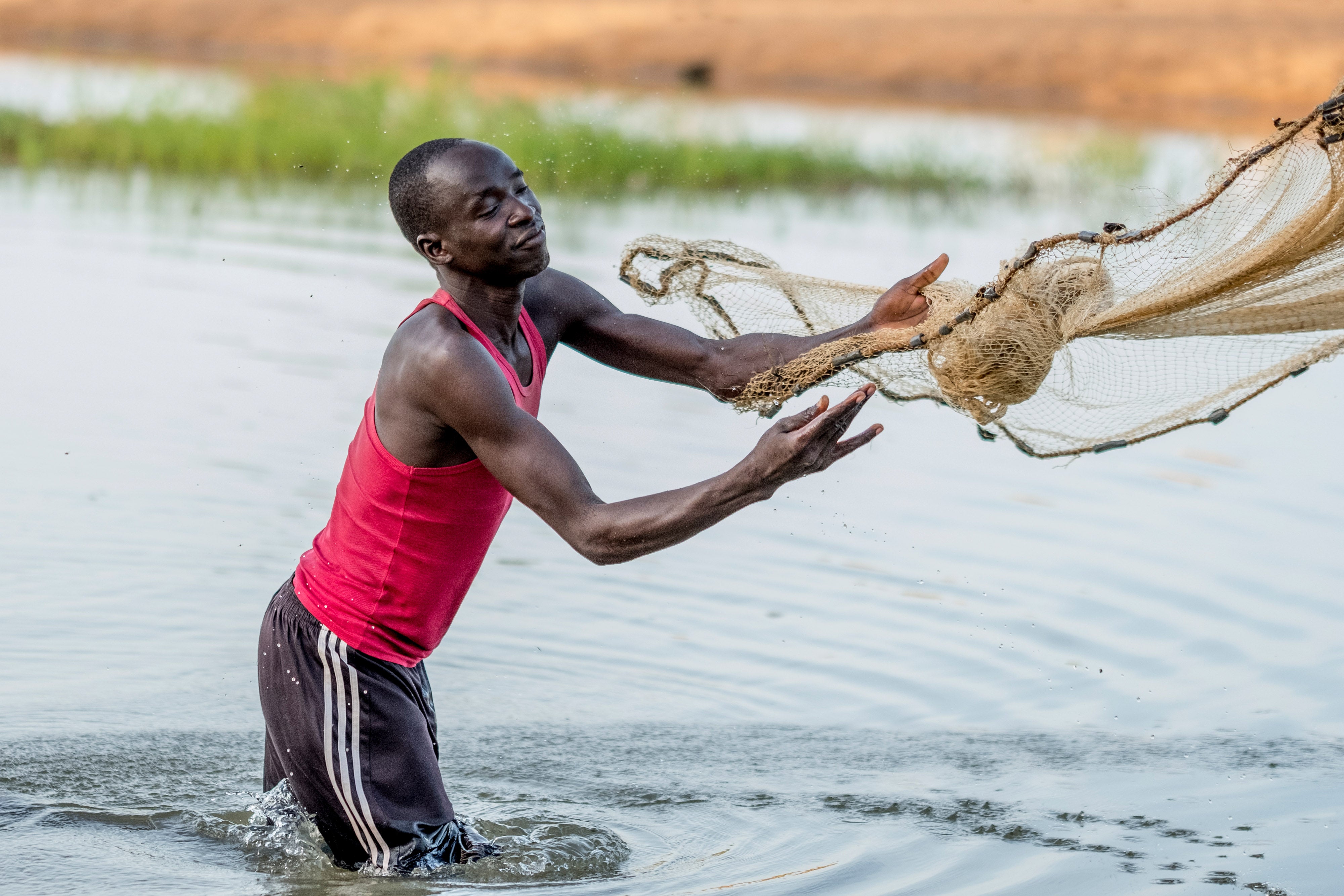 man standing in a pond throwing out a fishing net