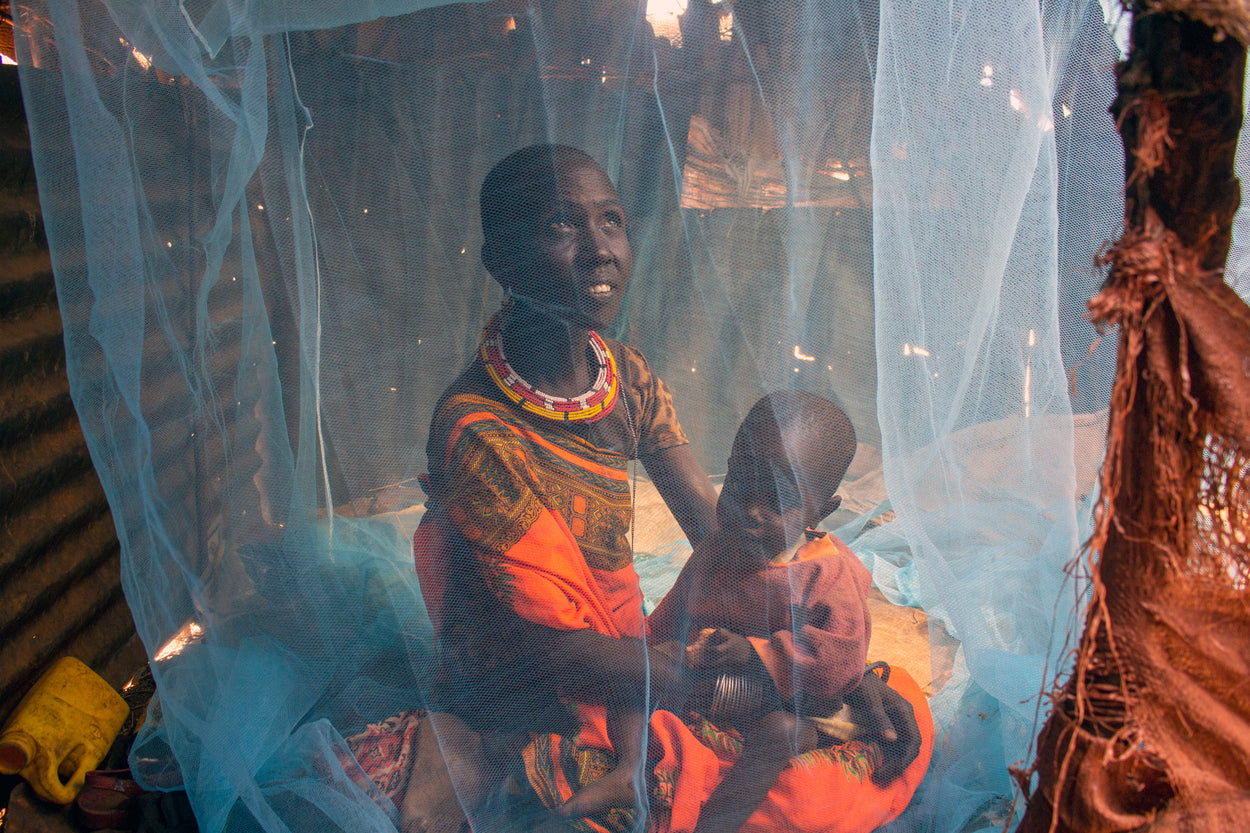 A mother and her baby sit underneath a mosquito net.