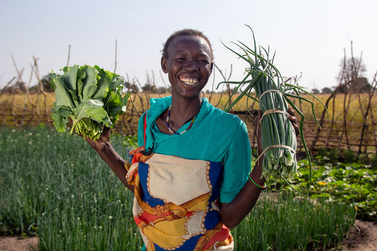 A woman smiles as she shows off the produce from her vegetable garden.