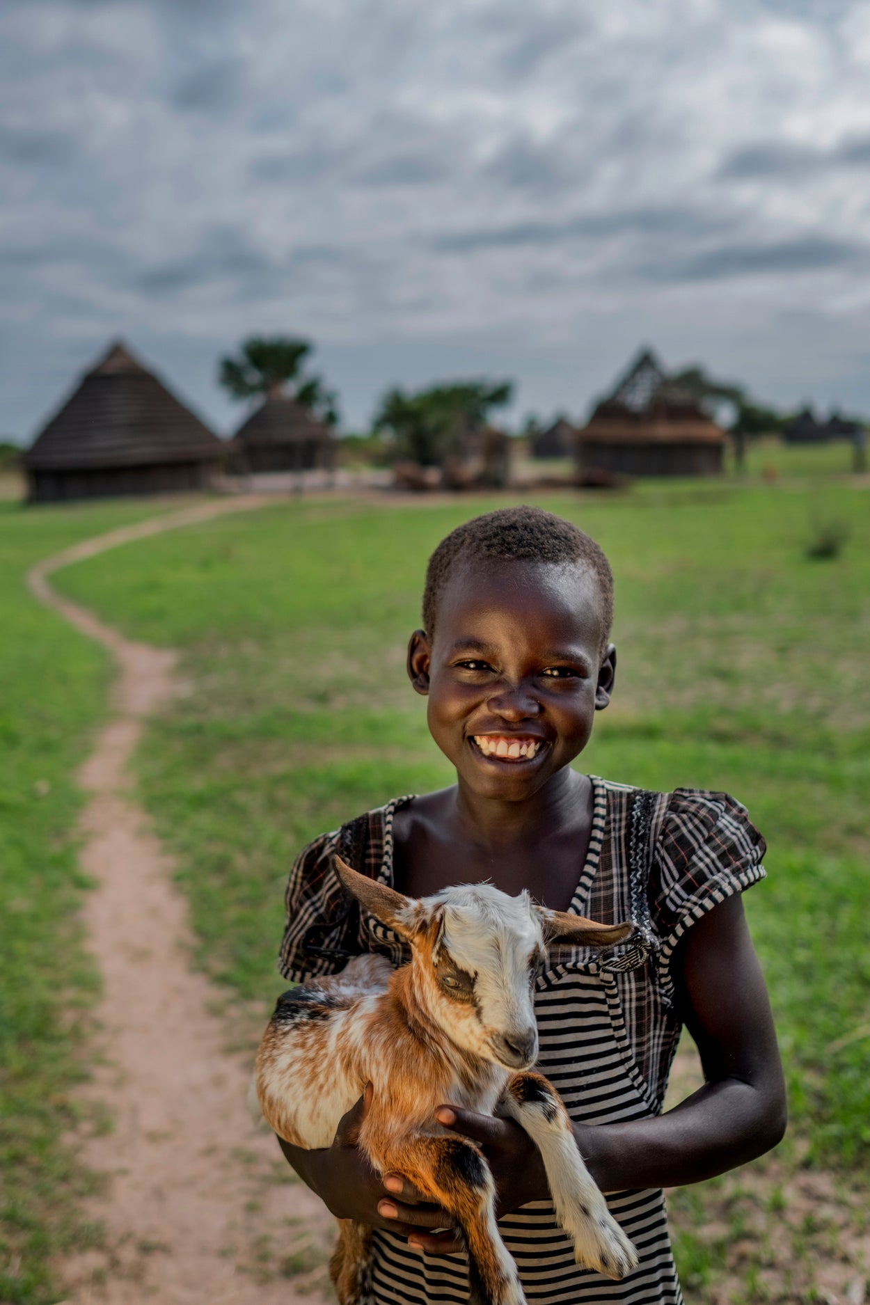 Girl holding a goat in front of a village road 