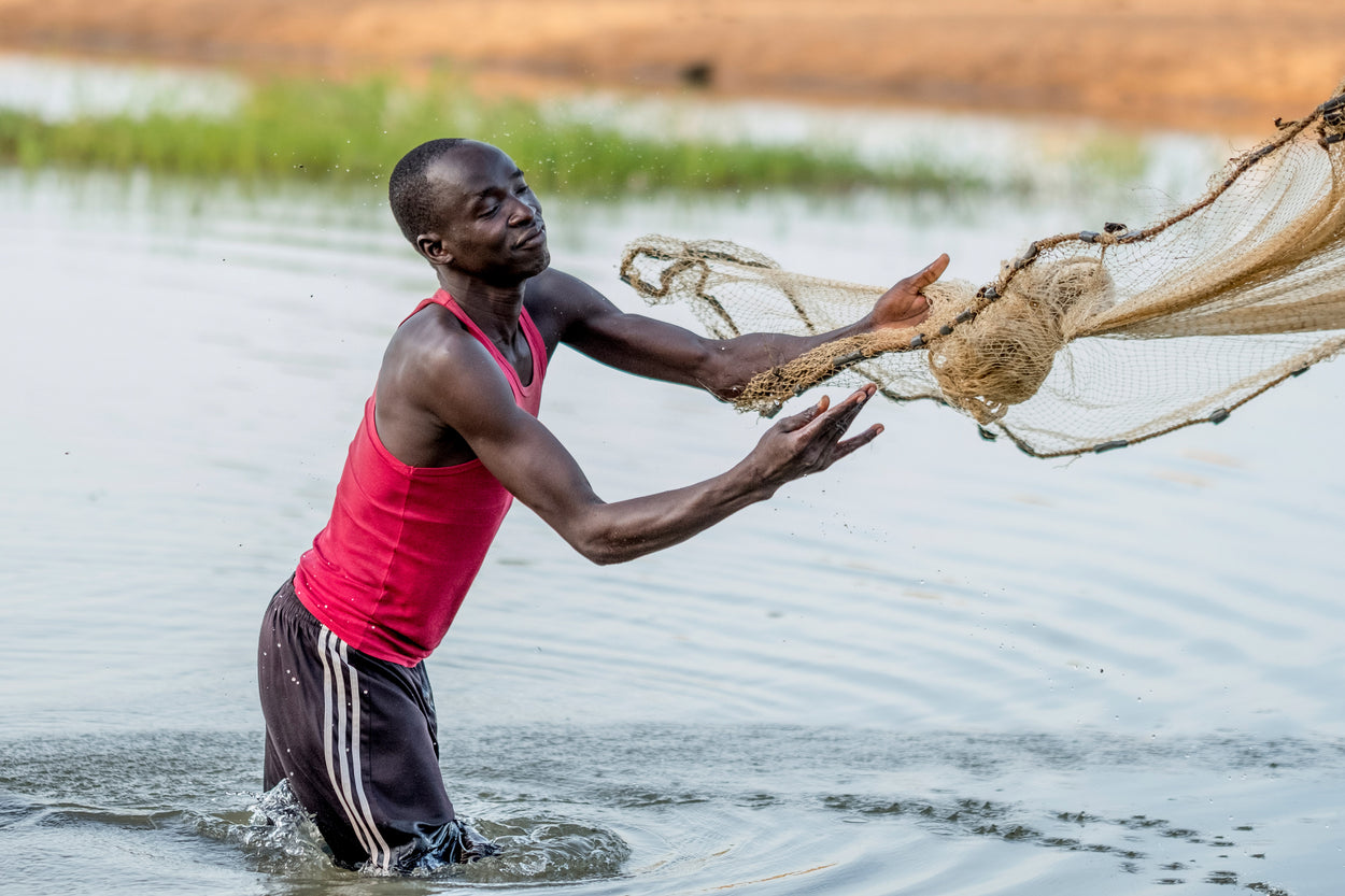 man standing in a pond throwing out a fishing net 