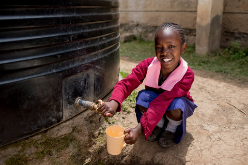 a girl sitting in front of a rainwater collection tank