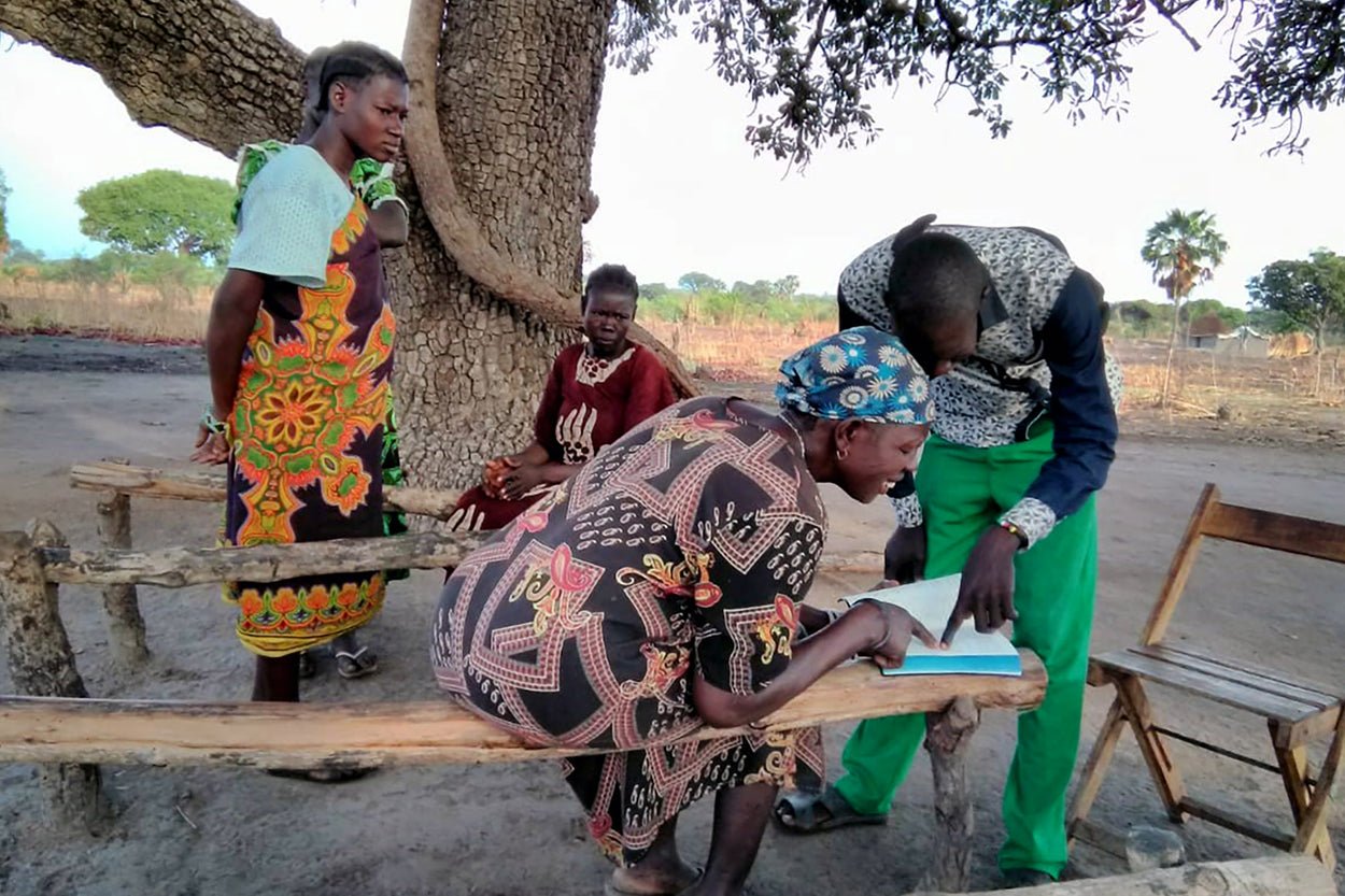 A woman smiles as she reads the Bible with the help of a local pastor.