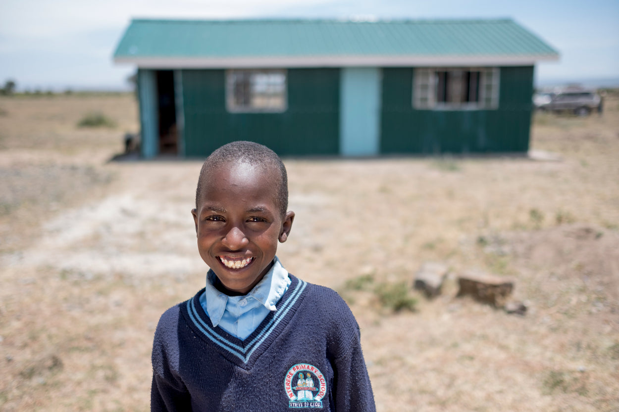 boy in a school uniform standing in front of a village classroom