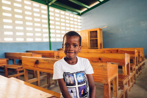 a little boy in a white shirt sitting in an empty classroom 