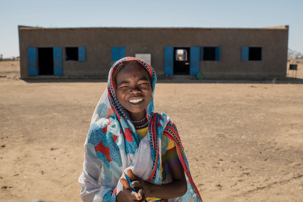 A young girl smiles as she stands in front of her classroom.